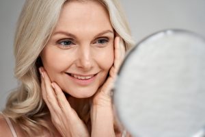 Smiling mature woman admiring her smooth complexion in the mirror after using medical-grade skincare